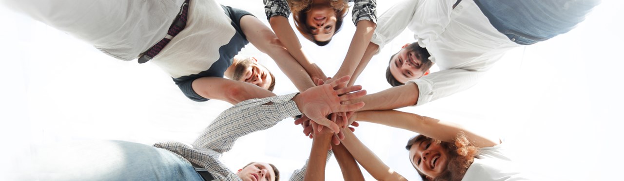 Eine Gruppe von Menschen, die in einem Kreis stehen und ihre Hände in der Mitte übereinandergelegt haben.