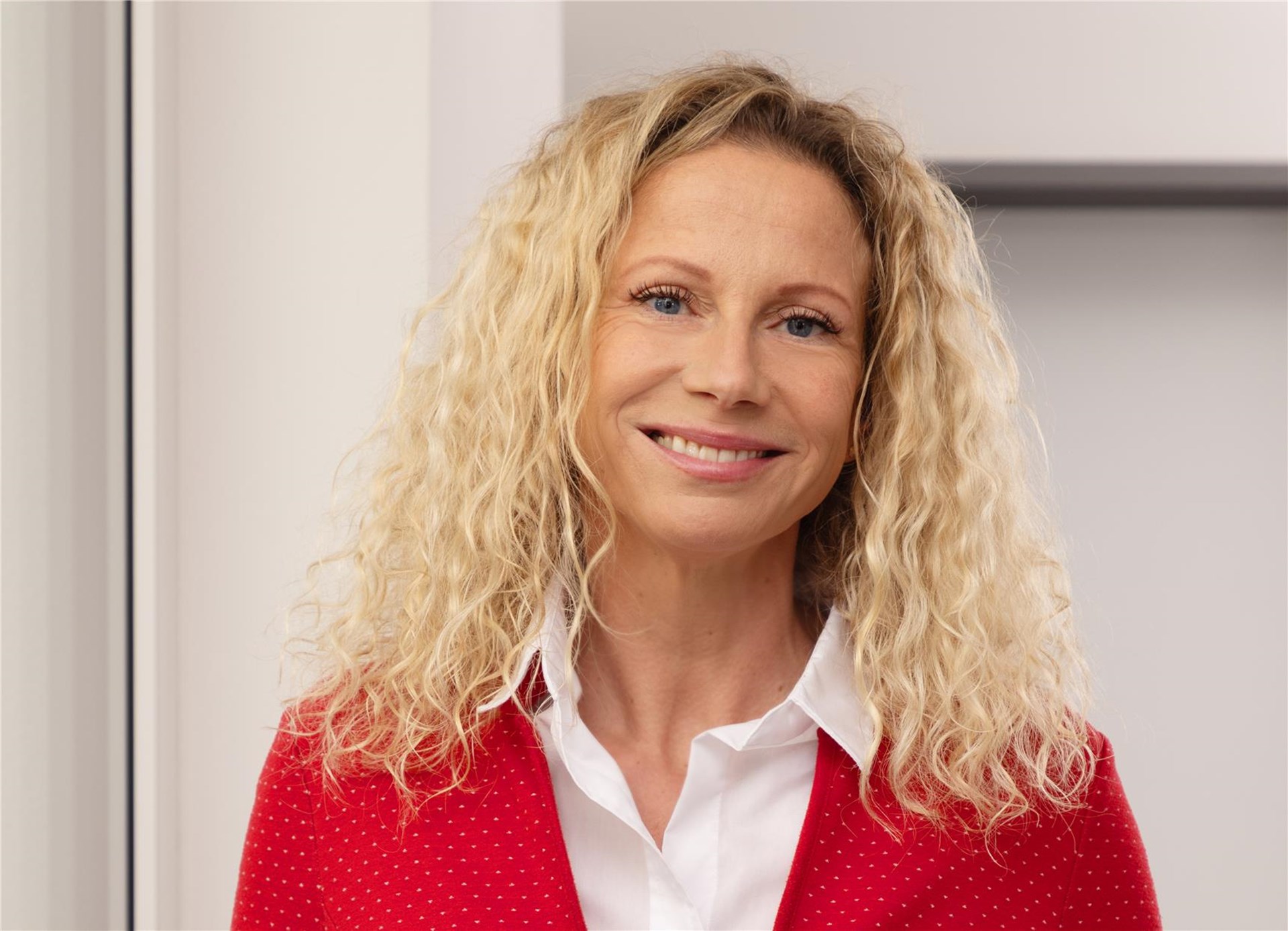 Frau mit langem blonden Haar und rotem Oberteil lächelt in die Kamera